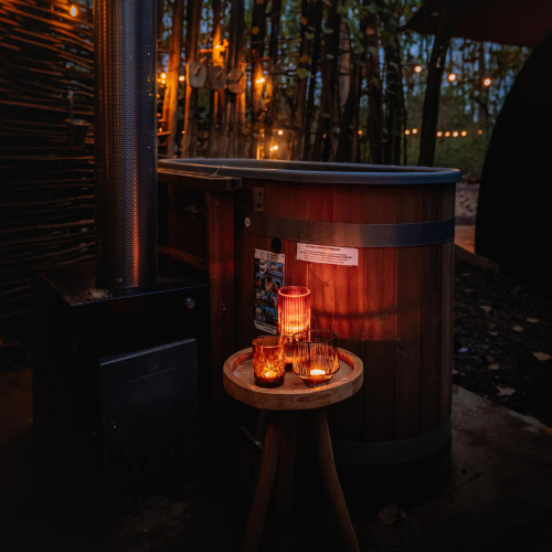 Buitenhottub en kaarslichttafel bij Boshuys tiny house op Buitengoed Ruysbos, Nederland, in de avond.