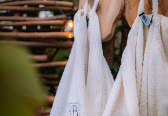 Twee witte badjassen hangen aan houten haken buiten bij Buitengoed Ruysbos, Boshuys, in Nederland.