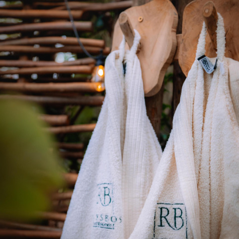 Two white bathrobes hang on wooden hooks outdoors at Buitengoed Ruysbos, Boshuys, in the Netherlands.