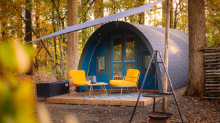 Kleines Haus mit gewölbtem Dach, gelbe Stühle und Terrasse im Wald bei Buitengoed Ruysbos, Niederlande.