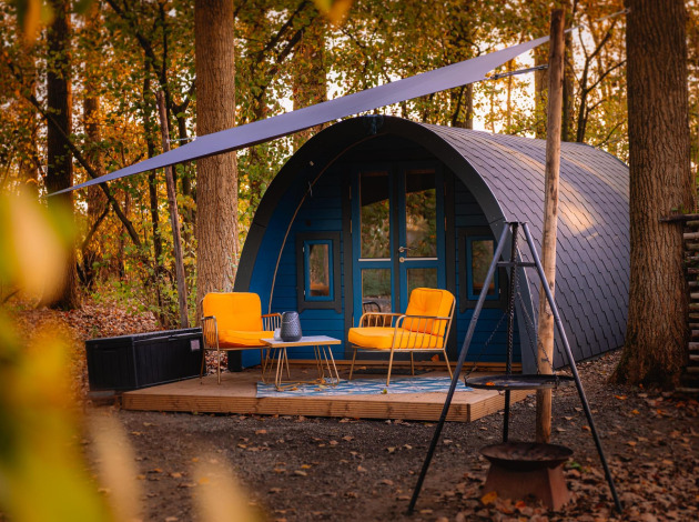 Tiny house met gebogen dak, gele stoelen en terras in het bos bij Buitengoed Ruysbos, Nederland.