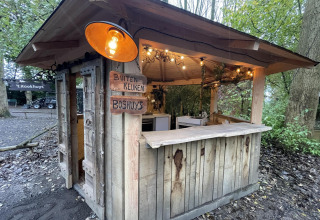 Una pequeña casa de madera con cocina al aire libre, carteles de madera y luces, en un área boscosa.