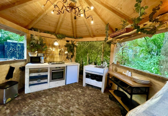 Acogedora cocina de casa pequeña con techo de madera, grandes ventanales y vista al bosque verde.