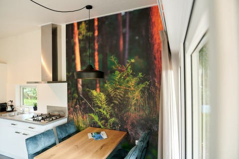 Moderne tiny house keuken met bosbehang, houten tafel en blauwe stoelen in Sand Lodge bij De IJsvogel.
