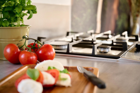 Frische Basilikum, Tomaten und Mozzarella auf einem Schneidebrett in einer Tiny House-Küche mit Gasherd.