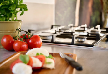 Albahaca fresca, tomates y mozzarella sobre una tabla en la cocina de una tiny house con estufa a gas al fondo.