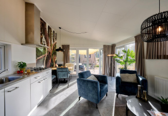Moderne tiny house-stue med åbent køkken, komfortable stole og store vinduer med udsigt til terrassen.