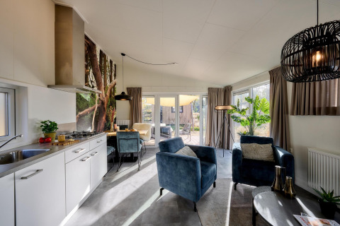 Moderne tiny house-stue med åbent køkken, komfortable stole og store vinduer med udsigt til terrassen.