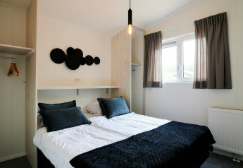 Modern bedroom inside the Sand Lodge tiny house at Holiday Park De IJsvogel, Netherlands, with double bed.