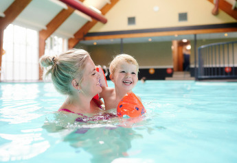 En mor og hendes lille barn nyder en svømmetur i poolen på Sand Lodge, Holiday Park De IJsvogel.