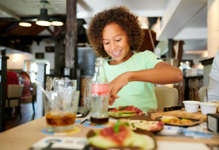 Bambino che mangia felice nella Sand Lodge, tiny house a Holiday Park De IJsvogel nei Paesi Bassi.