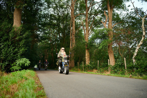 Gezin rijdt op elektrische scooters over een bosweg bij Sand Lodge in Holiday Park De IJsvogel, Nederland.