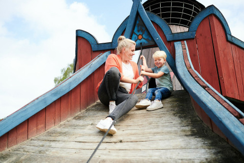 Madre e hijo juegan en un parque de madera en Sand Lodge del Holiday Park De IJsvogel en Países Bajos.