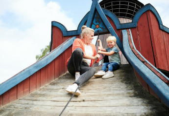 Madre e hijo juegan en un parque de madera en Sand Lodge del Holiday Park De IJsvogel en Países Bajos.