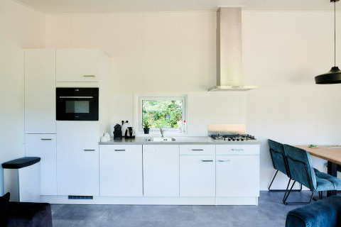 Moderne tiny house keuken met witte kasten, ingebouwde oven, gaskookplaat en gezellige eethoek.