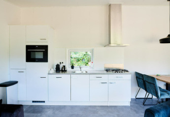 Cocina moderna de tiny house con armarios blancos, horno empotrado, estufa de gas y rincón comedor.