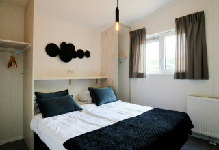 Dormitorio moderno y compacto en una tiny house con cama doble, armario abierto y ventana luminosa.