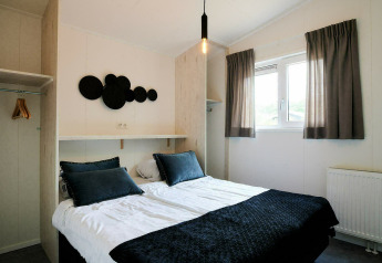 Moderne compacte slaapkamer in een tiny house met dubbel bed, open kast en een helder raam.
