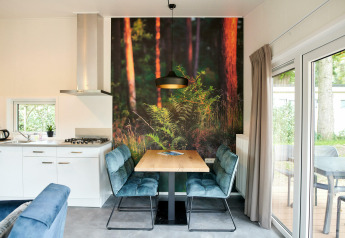 Moderne tiny house met eethoekje, boswanddecoratie, open keuken en grote ramen richting het terras.