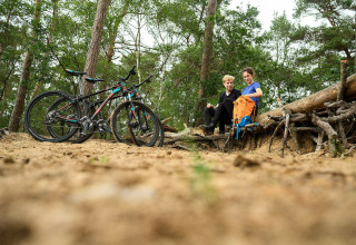 Twee mensen nemen pauze met hun fietsen in het bos bij Sand Lodge Sauna, De IJsvogel, Nederland.