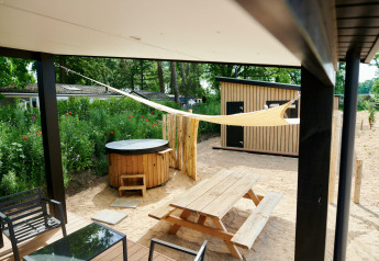 Udendørs terrasse med jacuzzi, træbord-bænkesæt og skyggefuldt sejl ved Sand Lodge i Holiday Park De IJsvogel.