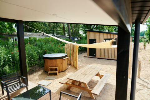 Udendørs terrasse med jacuzzi, træbord-bænkesæt og skyggefuldt sejl ved Sand Lodge i Holiday Park De IJsvogel.