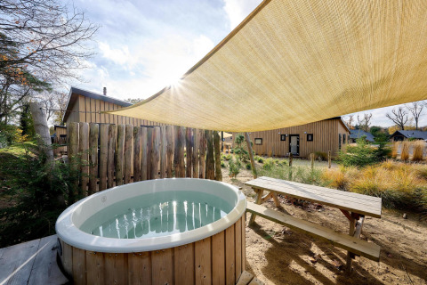 Udendørs jacuzzi og picnicbord ved Sand Lodge Jacuzzi, Holiday Park De IJsvogel, med solsejl og natur.