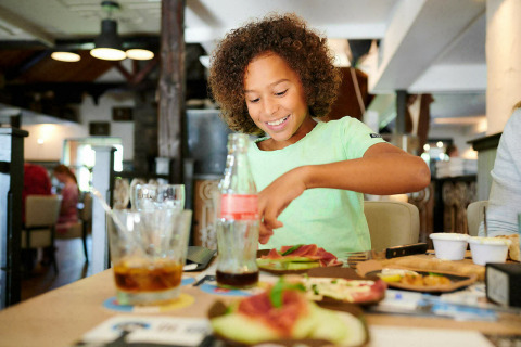 Kind geniet van maaltijd aan tafel in Sand Lodge Jacuzzi, Holiday Park De IJsvogel, Nederland, lichte sfeer.