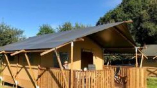 Safari telt på Camping O2 i Frankrig med træterrasse og tag, omgivet af grønt græs og blå himmel.
