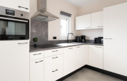 Modern white kitchen with black appliances and a window at Wood Lodge, Kompas Camping Nieuwpoort, Belgium.