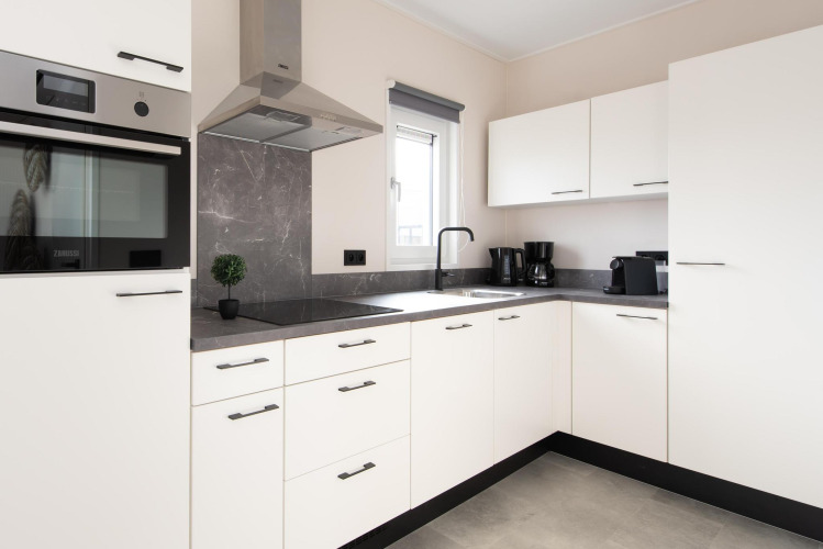 Moderne witte keuken met zwarte apparaten en raam in Wood Lodge op Kompas Camping Nieuwpoort, België.