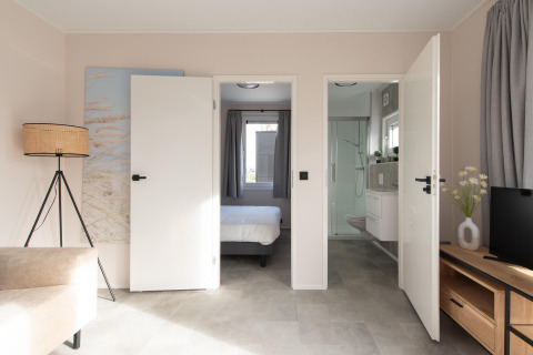 Indvendigt billede af Wood Lodge med åbne døre til soveværelse og badeværelse på Kompas Camping Nieuwpoort.