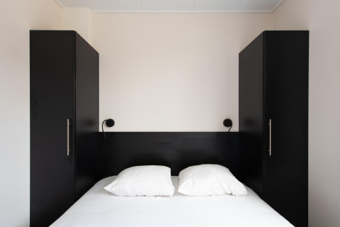 Camera moderna con letto matrimoniale, armadi neri e luci a muro al Wood Lodge, Kompas Camping Nieuwpoort.