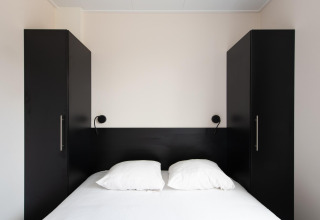 Camera moderna con letto matrimoniale, armadi neri e luci a muro al Wood Lodge, Kompas Camping Nieuwpoort.