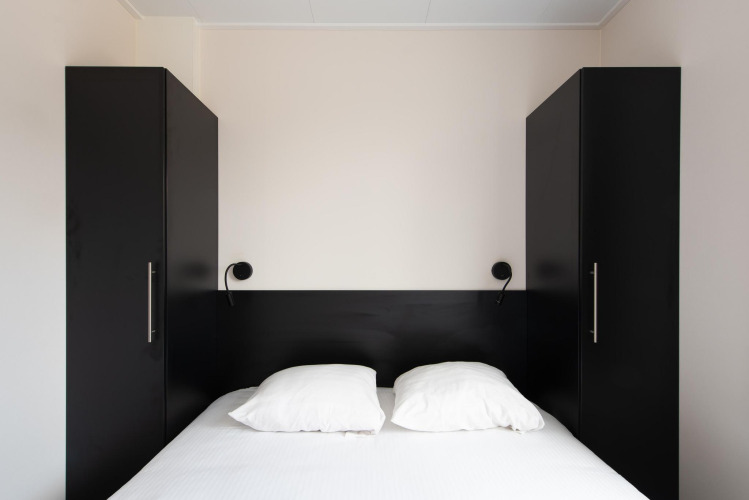 Chambre moderne avec lit double, armoires noires et lampes murales au Wood Lodge, Kompas Camping Nieuwpoort.
