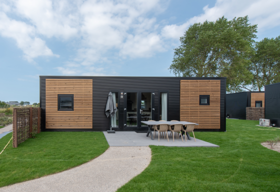 Cabaña moderna con fachada negra y madera, área de comedor exterior y césped verde bien cuidado al frente.
