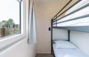Interieur van een kamer met stapelbed en groot raam in Wood Lodge, Kompas Camping Nieuwpoort, België.