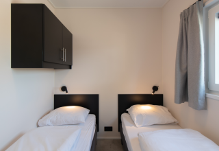 Habitación sencilla de lodge con dos camas individuales, armario negro, luces de pared y ventana cortinada.