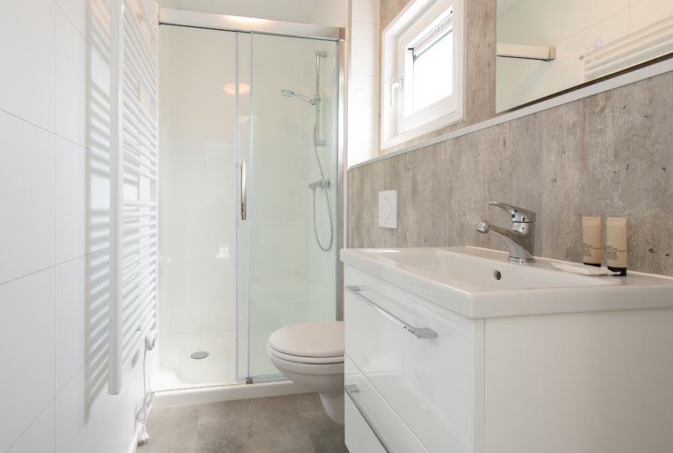 Baño moderno en lodge con ducha acristalada, lavabo blanco, inodoro y decoración minimalista.
