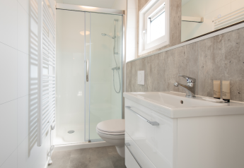 Modern lodge bathroom with glass shower, white sink, toilet, mirror and minimalist interior decor.