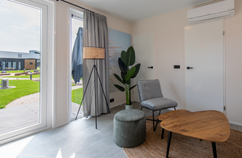 Moderne lodge stue med store vinduer, minimalistiske møbler, grøn plante og udsigt til have.