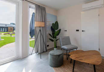 Moderne lodge stue med store vinduer, minimalistiske møbler, grøn plante og udsigt til have.