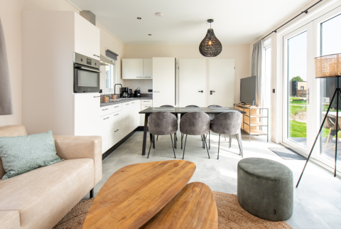 Modern lodge interior featuring an open kitchen, dining table with six chairs, and large windows.