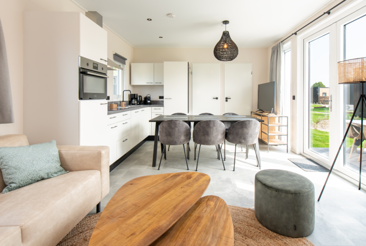 Modern lodge interior featuring an open kitchen, dining table with six chairs, and large windows.