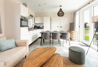 Intérieur de lodge moderne avec cuisine ouverte, table à manger pour six et grandes baies vitrées.