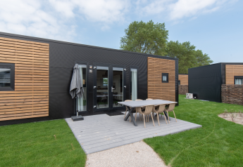 Modern lodge with black and wood paneling, outdoor dining area, and green lawn under a partly cloudy sky.
