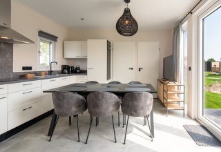Modern lodge kitchen and dining area with grey chairs, large windows, and garden view in sunlight.