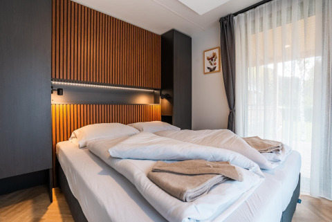 Moderne slaapkamer in Enzian Hottub bij Ossiacher See in Oostenrijk met tweepersoonsbed en houten wandpanelen.
