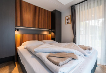 Chambre moderne à Enzian Hottub au lac Ossiacher en Autriche avec lit double, boiseries et grandes fenêtres.