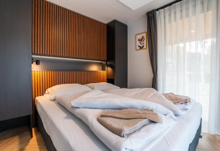 Moderne slaapkamer in Enzian Hottub bij Ossiacher See in Oostenrijk met een dubbel bed en houten wanddetails.